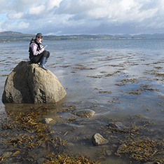 woman taking notes sitting on a rock surrounded by the sea