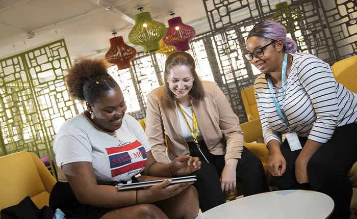 Three smiling people on comfy sofas looking at a tablet together
