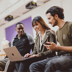Three students sitting with a laptop of one of their knees