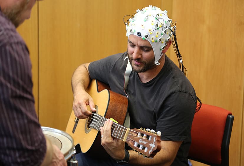 Research participant wearing wearing a headpiece that monitors brain activity, while playing the guitar