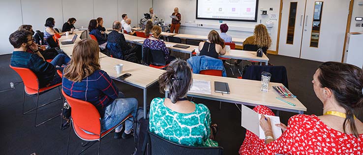 Back view of academics sitting at tables in a seminar room, listening to a talk