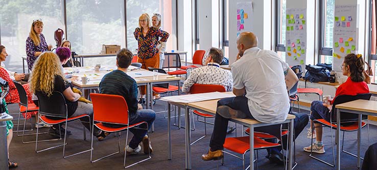 Back view of academics sitting on chairs and tables in a seminar room, in a workshop