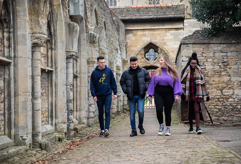 A group of four students walking down a medieval street near Peterborough Cathedral