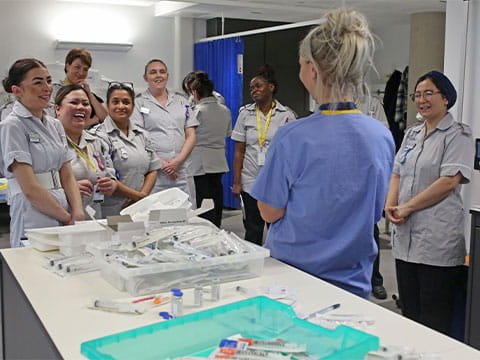 A class of healthcare students with their lecturer, near a table full of syringes