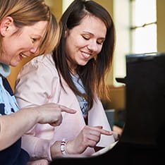 A woman teaching another how to play piano