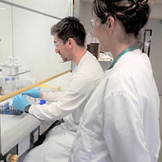 Two scientists in white coats at a bench in the biomarker lab