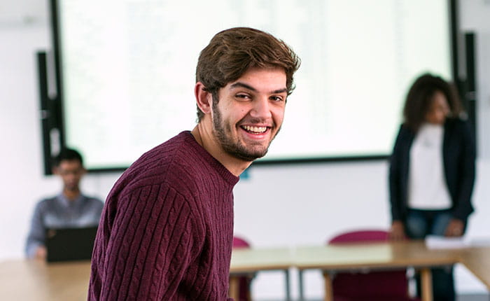 Three students in a university classroom, one in foreground and two in the background