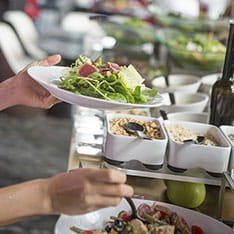 A pair of hands holding a plate of salad and adding more to the plate from a buffet
