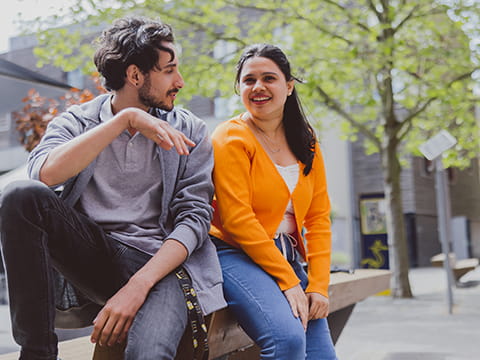 A male and a female student talk, whilst sat in the Cambridge campus quad