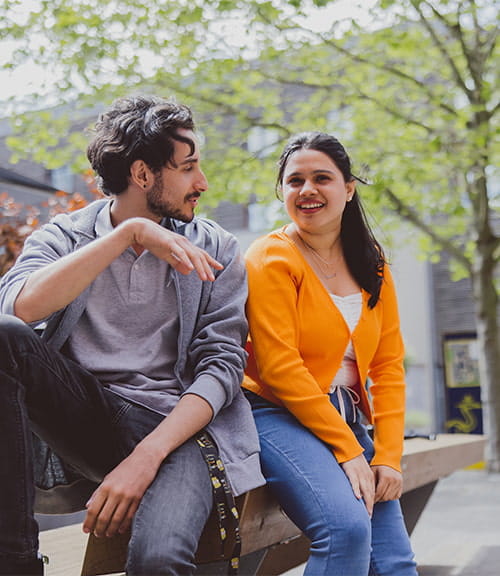A male and a female student talk, whilst sat in the Cambridge campus quad