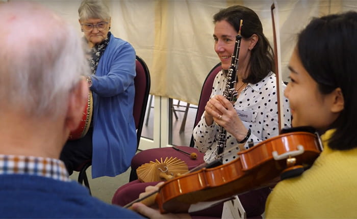 Older people in a music therapy session with a violinist and a clarinettist