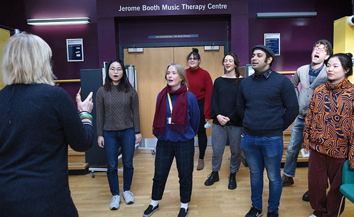 Seven people and a music therapist singing in the lobby of the Jerome Booth Music Therapy Centre in Cambridge