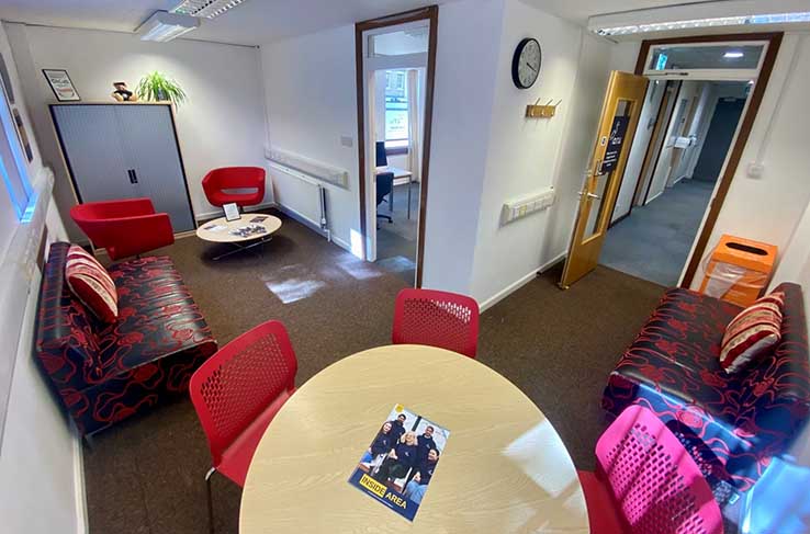 View of part of the AREA CoLab in Cambridge, with chairs and tables, sofas, a cabinet, and doors to a co-working space and a corridor