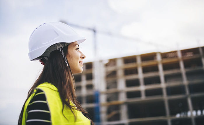 A woman in high viz and a hard hat with a building site in the background