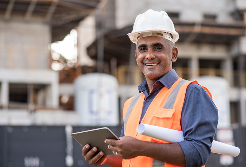 A man on a construction site, wearing hi viz and a hard hat and holding a tablet