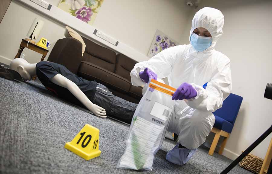 A Forensics student practising bagging up evidence, with a dummy lying face-down in the background