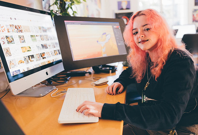 A student working at a Mac with two screens