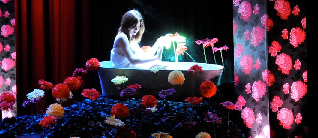 Theatre set of a woman in a bathtub on a mound of flowers