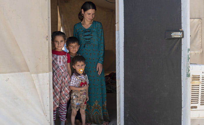 A Yazidi mother and three children standing in the doorway of makeshift accommodation