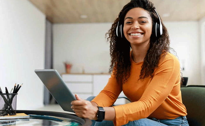 A student sitting at a coffee table wearing headphones and using a tablet
