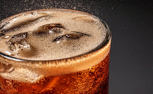 Close-up of the top of a glass of cola with ice and lemon, with fizzy bubbles jumping off the surface