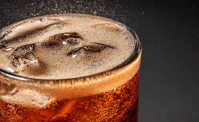 Close-up of the top of a glass of cola with ice and lemon, with fizzy bubbles jumping off the surface