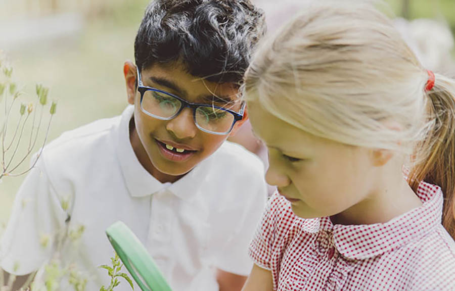 Two schoolchildren looking through a magnifying glass in a green space