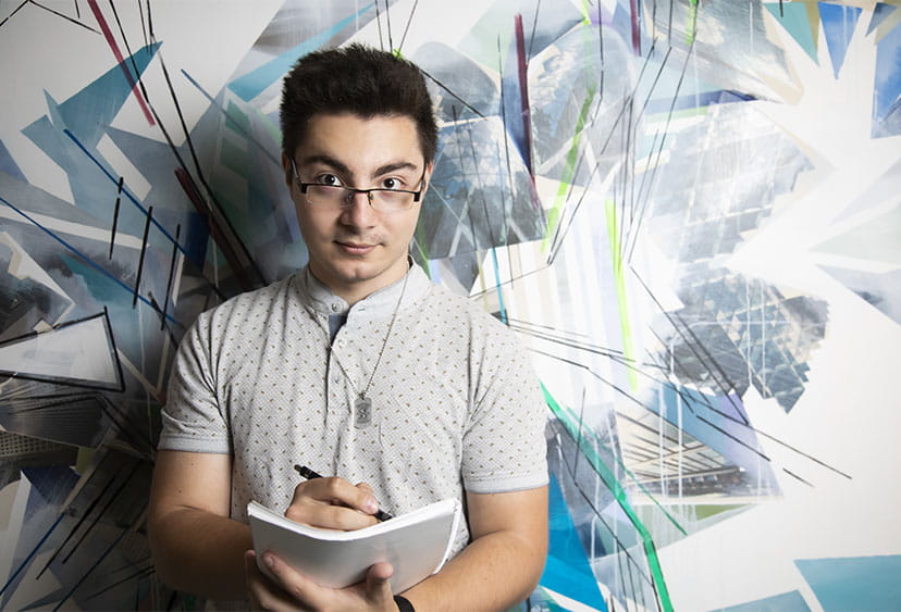 Someone standing while writing notes and looking at the camera