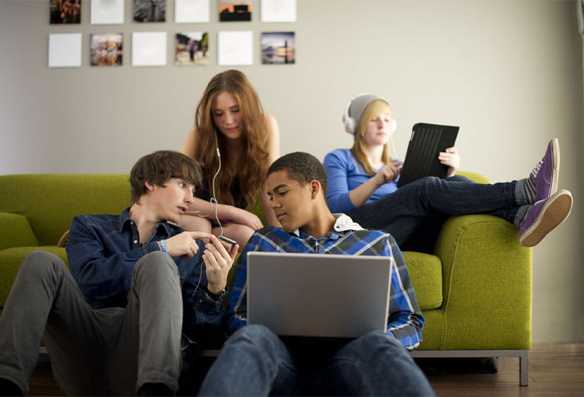 Teenagers lounging around a sofa sharing looks at one of their mobile phone screens