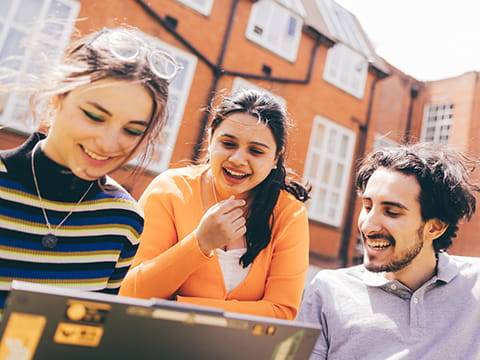 A group of students look at a laptop in the Cambridge campus grounds