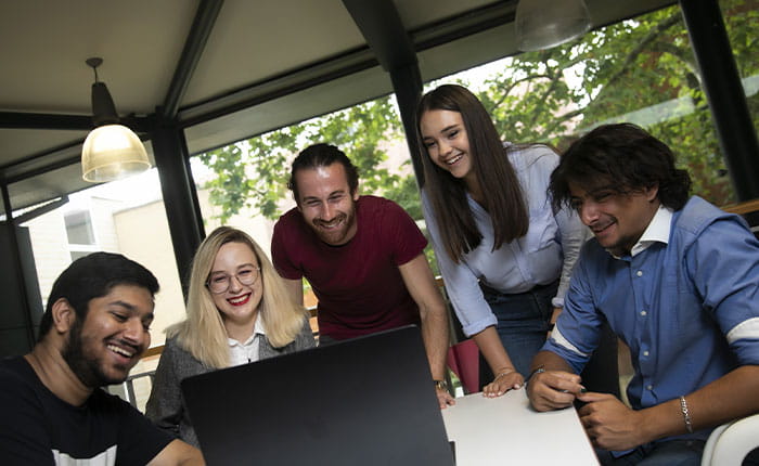Five students huddled around a laptop