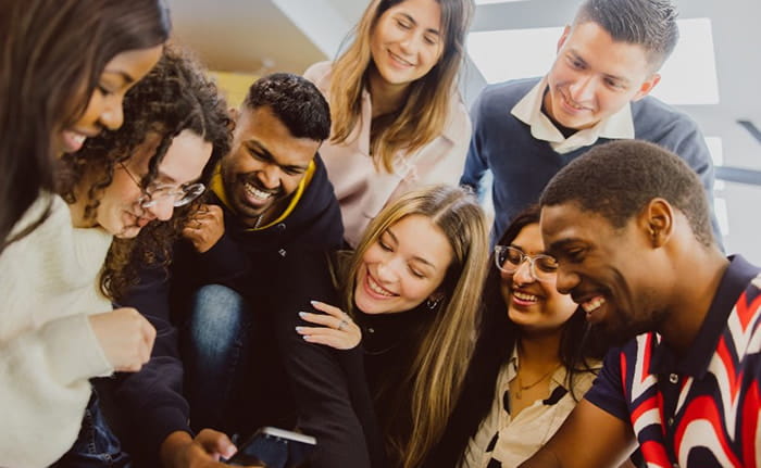 A group of international students look and laugh whilst looking at a mobile device