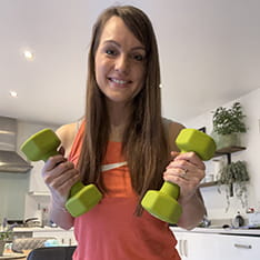 Hannah Impey holding up a pair of weights in her kitchen