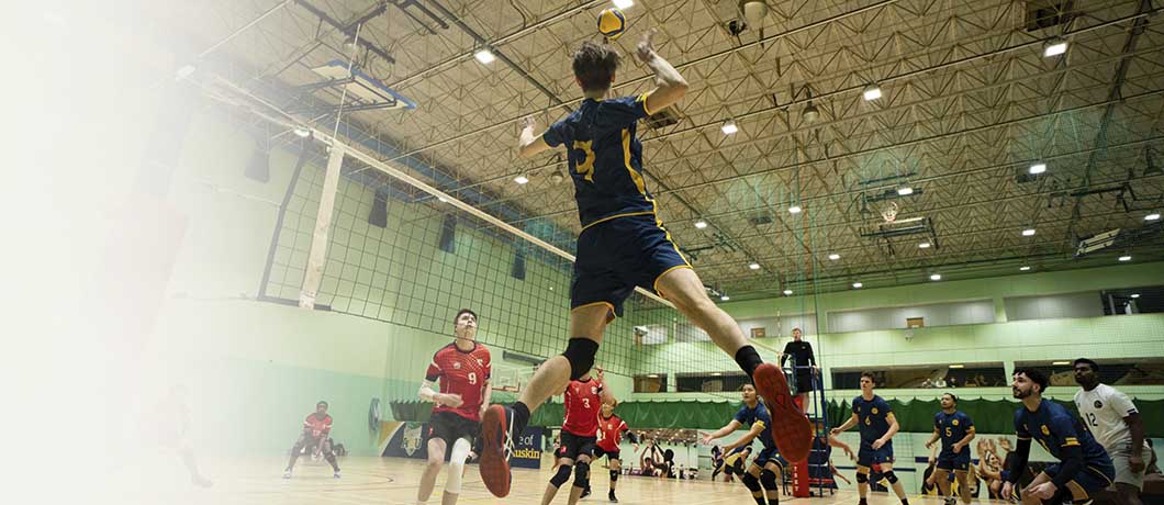 ARU students, one mid-jump playing volleyball in the sports hall