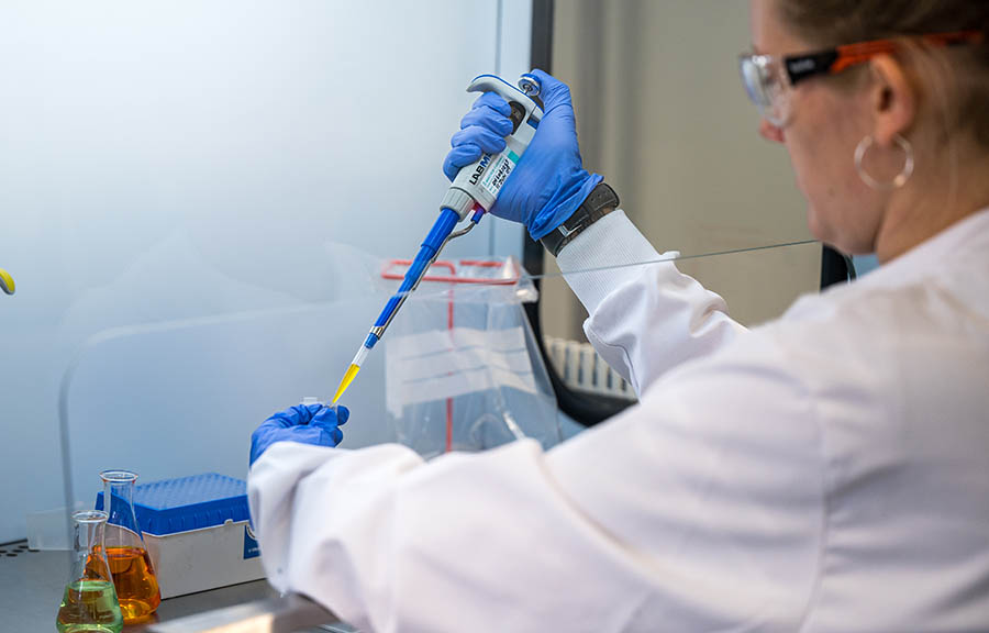 Back view of a forensic scientist pipetting liquid into a container in a fume cabinet