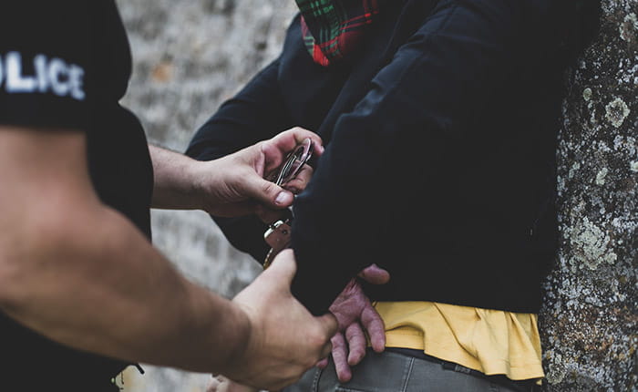 A man with his hands behind his back being handcuffed by a police officer