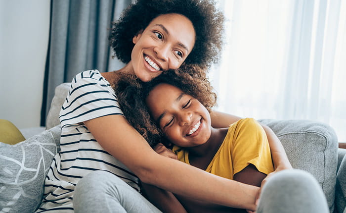 A woman and a young girl smiling and hugging on a sofa