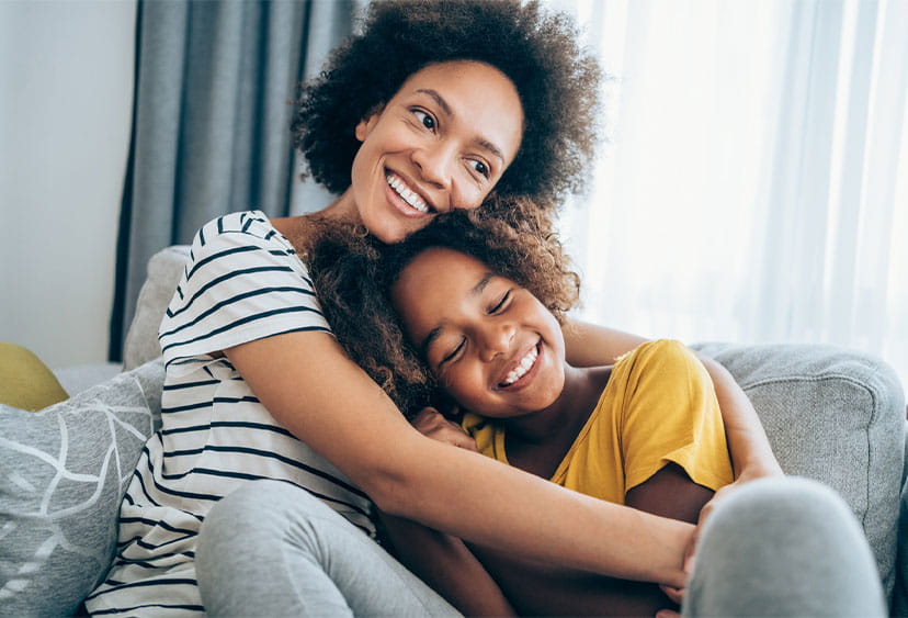 An adult and a child cuddling on a sofa, smiling