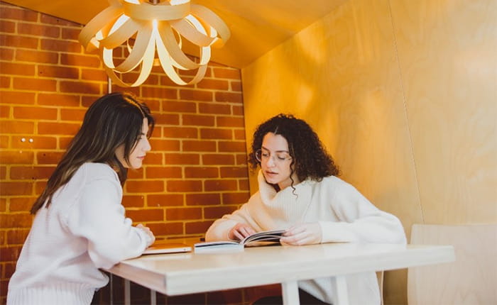 Two international students discuss work at a table