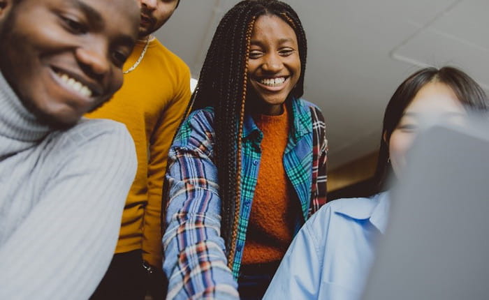 Four international students discuss work and look at a desktop computer