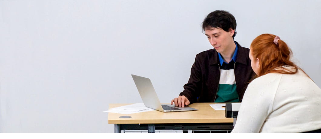 A man on a reception desk looking at a laptop with a female client