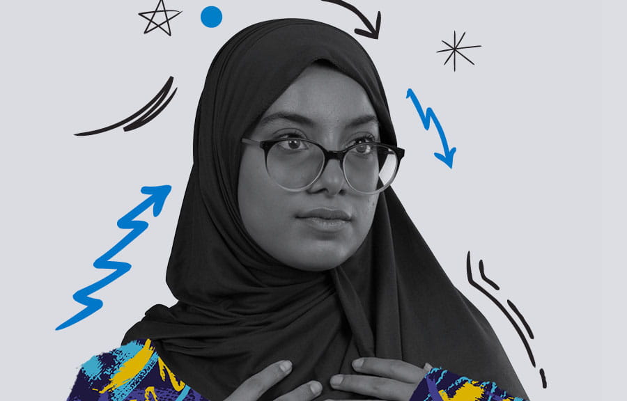 A student posing with her hands on the front of her hijab. Her top and the area around her are coloured with yellow and blue patterns and squiggles.