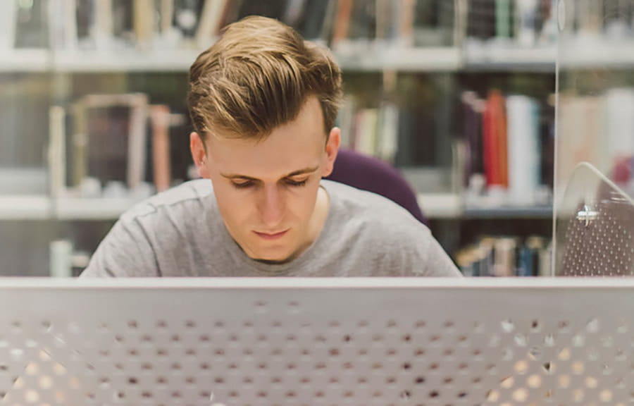 A student working in front of shelves of books in a library