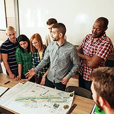 A group of people in a classroom, gathered around a plan