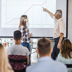 A man and woman work on an interactive whiteboard in front of an audience