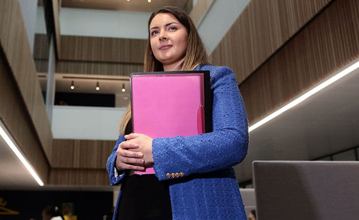 A student standing, holding a folder, in the main area of University House, ARU Peterborough