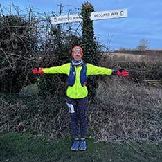 Michelle Berry posing in hi-viz running gear in front of a sign pointing to Peddars Way