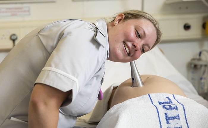 A Midwifery student using an instrument to listen to a dummy pregnancy bump