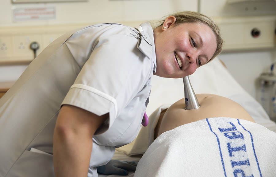 A Midwifery student using an instrument to listen to a dummy pregnancy bump