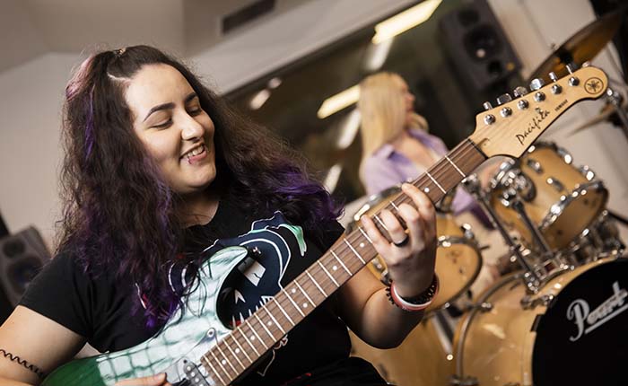 Two music students in a recording student, one playing guitar and the other drums